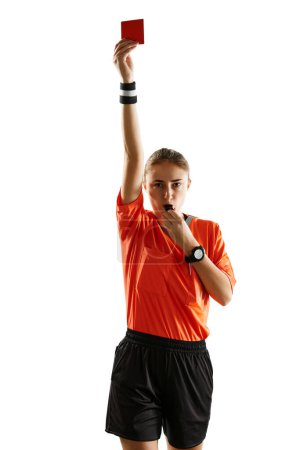 Photo for Young concentrated woman, soccer referee blowing a whistle and showing red card as dismissal symbol against white studio background. Concept of sport, competition, match, profession, control - Royalty Free Image