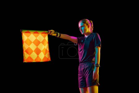 Photo for Young woman, assistant referee raising flag up meaning offside position against black studio background in neon light. Concept of sport, competition, match, profession, football game, control - Royalty Free Image