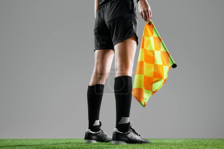 Photo for Legs of female referee in sportswear standing with flag, signaling for an offside on the near side of the field against grey background. Concept of sport, competition, match, profession, football game - Royalty Free Image