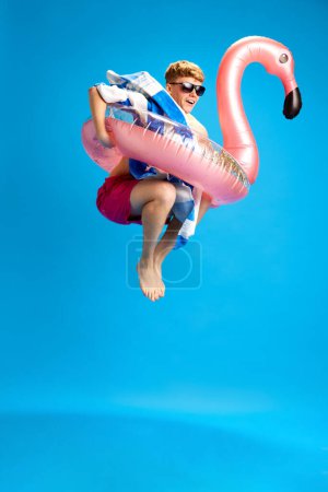 Foto de Joven chico relajado alegre en el círculo de natación disfrutando de viaje de verano, divertirse contra fondo estudio azul. Concepto de emociones, juventud, tiempo libre, vacaciones de verano - Imagen libre de derechos