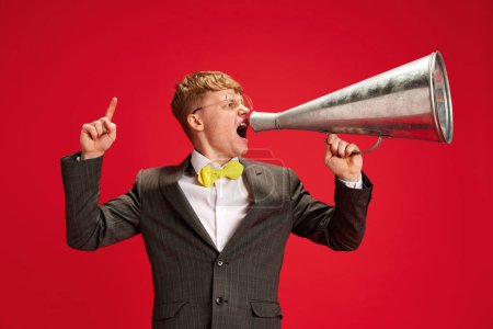 Photo for Young emotional man in formal wear, employee talking in megaphone against red studio background. Important announcement. Concept of business, youth, human emotions, lifestyle - Royalty Free Image