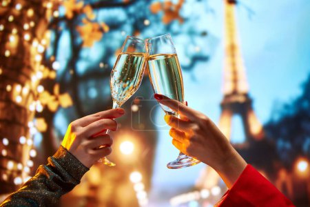 Photo for Female hands clinking champagne glasses over beautiful view of France poplar landmark. Celebrating birthday. Travel agency ad for exclusive Paris tours. Concept of holidays, celebration - Royalty Free Image