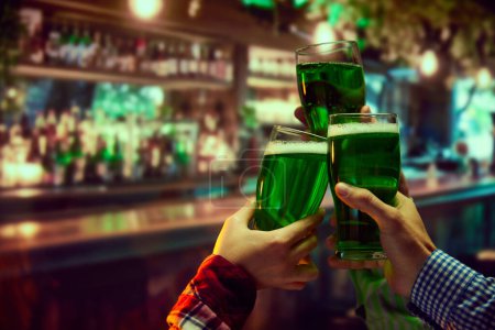 Photo for St. Patricks Day celebration promotion at a local bar or pub. Human hands clinking mugs filled with green beer. Traditional holiday. Concept of holidays, celebration, events - Royalty Free Image