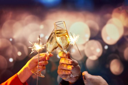 Photo for Romantic date night experience service, complete with champagne and sparklers. Two hands holding champagne glasses with sparklers over bokeh lights background. Concept of holidays, celebration, events - Royalty Free Image