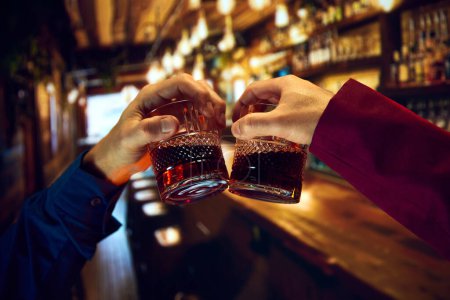 Foto de Manos masculinas, hombres de negocios tintineando vasos de whisky, encontrándose en el pub, restaurante. Reunión de amigos. Concepto de vacaciones, celebración, eventos - Imagen libre de derechos