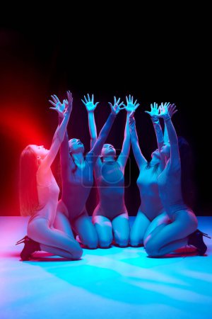 Téléchargez les photos : Jeune femme, danseuses professionnelles en body dansant à talons hauts sur fond noir au néon. Concept de style de danse moderne, créativité et beauté, art, passe-temps - en image libre de droit