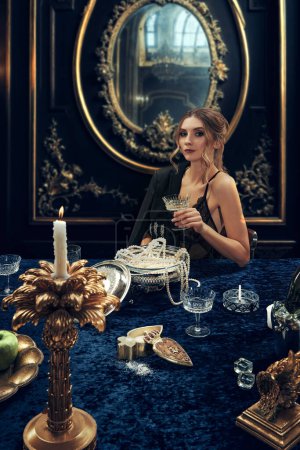 Photo for Portrait of elegant beautiful young serious woman in luxurious dark costume raising glass with champagne. Wealthy lifestyle of youth. Concept of upper-class, holidays, party, royalty - Royalty Free Image