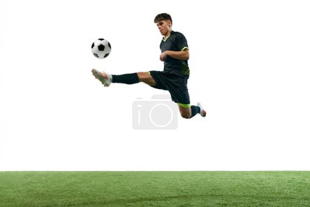 Foto de Imagen dinámica del joven, fútbol jugando en movimiento, jugando aislado sobre fondo blanco con suelo de hierba. Concepto de deporte, juego, competición, campeonato, estilo de vida activo - Imagen libre de derechos