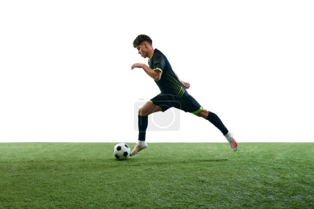 Photo for Young man, football player in motion during game, running with ball isolated over white background with grass flooring. Concept of sport, game, competition, championship, active lifestyle - Royalty Free Image
