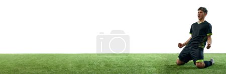 Foto de Joven, futbolista mostrando emociones de victoria, sentado en el suelo aislado sobre fondo blanco con suelo de hierba. Concepto de deporte, competición, estilo de vida activo. Banner. Espacio vacío para insertar texto - Imagen libre de derechos