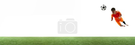 Photo for Young man, football player in orange hitting ball in a jump with head isolated over white background with grass flooring. Concept of sport, game, competition, championship, active lifestyle. Banner - Royalty Free Image