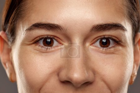 Foto de Primer plano de las mujeres ojos marrones, sin maquillaje mirando a la cámara. Cuidado de la salud, visión. Mujer sonriendo. Concepto de belleza natural, cosmetología y cosmética, cuidado de la piel - Imagen libre de derechos