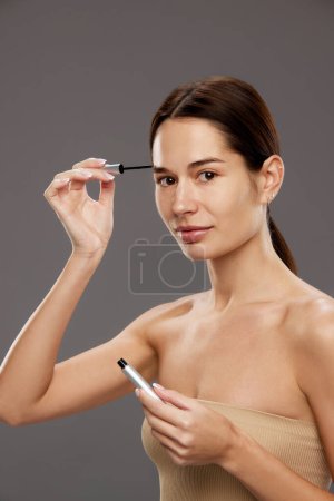 Photo for Tutorial on makeup techniques for enhancing natural beauty. Woman holding brow fixing gel against studio background against background. Concept of natural beauty, cosmetology and cosmetics, skin care - Royalty Free Image