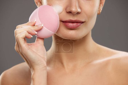 Photo for Young woman taking care after skin, washing face with foam and washing tool for deep pore cleansing against studio background. Concept of natural beauty, cosmetology and cosmetics, skin care - Royalty Free Image
