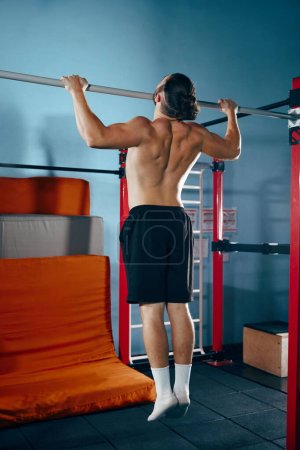 Téléchargez les photos : Jeune homme athlétique avec entraînement musculaire du corps torse nu, faire des exercices de traction dans la salle de gym moderne. Concept de mode de vie actif et sain, soins du corps, fitness, sport. Promotion de l'espace fitness - en image libre de droit