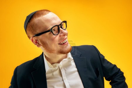 Photo for Portrait of smiling, happy young Jewish man in yarmulke, glasses and suit standing against yellow studio background. Concept of Purim holiday, Jewish traditions, history and culture - Royalty Free Image