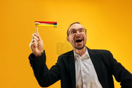 Photo for Jewish man in his 30s, in glasses, yarmulke joyfully posing with wooden noisemaker, gragger against yellow studio background. Concept of Purim holiday, Jewish traditions, history and culture - Royalty Free Image