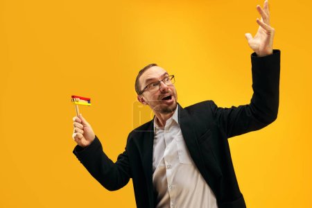 Photo for Jewish man in his 30s, in glasses, yarmulke joyfully posing with wooden noisemaker, gragger against yellow studio background. Concept of Purim holiday, Jewish traditions, history and culture - Royalty Free Image