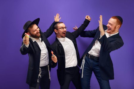 Photo for Enjoyment. Three Jewish men, friends in traditional Jewish attributes smiling, posing against against purple studio background. Concept of Purim holiday, Jewish traditions, history and culture - Royalty Free Image