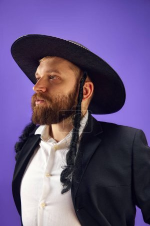 Photo for Portrait of bearded young Jewish man in hat, with sidelocks posing against purple studio background. Concept of Purim holiday, Jewish traditions, history and culture - Royalty Free Image