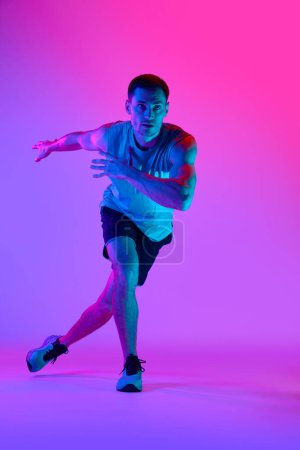Téléchargez les photos : Homme sportif en tenue de sport confortable, avec entraînement musculaire du corps sur fond rose dégradé dans la lumière néon. Concept de mode de vie actif et sain, sport, fitness, endurance - en image libre de droit