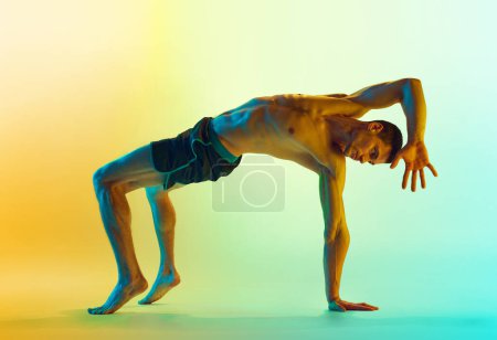 Photo for Intensive full-body training. Muscular athletic young shirtless man, with fit body doing workout exercises against gradient blue yellow background in neon. Active and healthy lifestyle, sport concept - Royalty Free Image