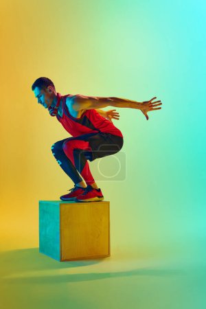 Photo for Full-length dynamic image of y9ung muscular man training, jumping on block, training against gradient blue yellow background in neon light. Concept of active and healthy lifestyle, sport, fitness - Royalty Free Image