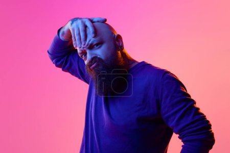 Photo for Gel portrait of bearded bald man in blue sweater expressing emotions, grimacing against pink background in neon light. Concept of human emotions, facial expression - Royalty Free Image