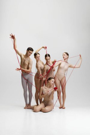 Photo for Tangled situation and assistance. Group of young people, ballet dancers sitting on floor with red tangled string against white studio background. Concept of classical dance, modern style, inspiration - Royalty Free Image