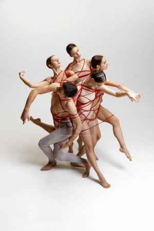 Foto de Talentosos jóvenes artísticos, hombres y mujeres, bailarines de ballet actuando, atados con cuerdas rojas, bailando sobre fondo blanco del estudio. Concepto de danza clásica, estilo moderno, inspiración - Imagen libre de derechos