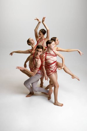 Téléchargez les photos : Groupe de danseurs de ballet, attachés ensemble avec des cordes rouges, créant pose complexe sur fond de studio blanc. Équilibre et harmonie. Concept de danse classique, style moderne, inspiration - en image libre de droit