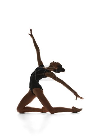 Téléchargez les photos : Adolescente tendre, gymnaste rythmique en costume noir se produisant, dansant sur fond de studio blanc. Concept de sport, beauté et grâce, compétition, art, jeunesse, hobby - en image libre de droit