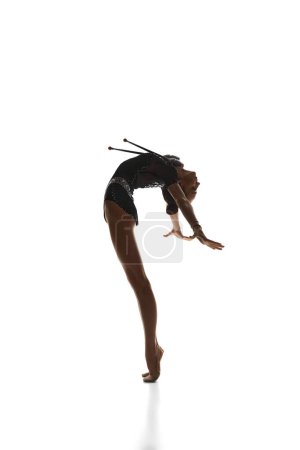 Téléchargez les photos : Élégance dans les mouvements. Belle adolescente, gymnaste rythmique en costume de scène noire dansant, se produisant sur fond de studio blanc. Concept de sport, beauté, grâce, compétition, art, jeunesse, hobby - en image libre de droit