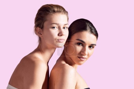 Photo for Portrait of beautiful brunette and blonde girls with well-kept skin, nude makeup, bare shoulders against pink studio background. Concept of natural beauty, cosmetology and cosmetics, skincare - Royalty Free Image