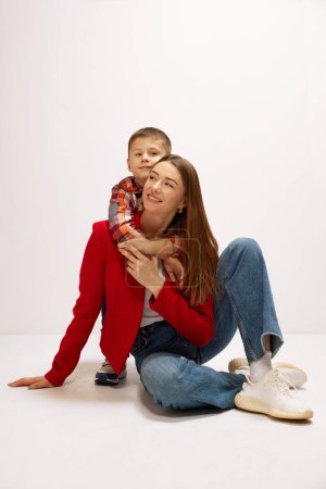 Foto de Retrato de una joven hermosa y sonriente, madre posando con su pequeño hijo, adorable niño sobre fondo blanco del estudio. Concepto de felicidad, Día de las Madres, infancia, moda y estilo de vida - Imagen libre de derechos
