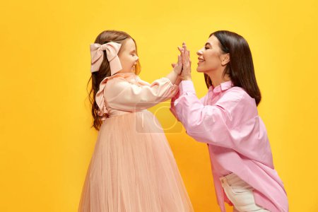 Photo for Mothers support and care. Happy family, mother and daughter holding hands and smiling to each other on yellow studio background. Concept of happiness, Mothers day, childhood, fashion and lifestyle - Royalty Free Image
