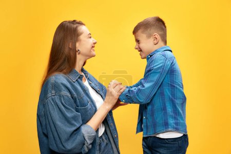 Foto de Mujer joven feliz, alegre, sonriente, madre jugando con su pequeño hijo sobre fondo amarillo del estudio. Concepto de felicidad, Día de las Madres, infancia, moda y estilo de vida - Imagen libre de derechos