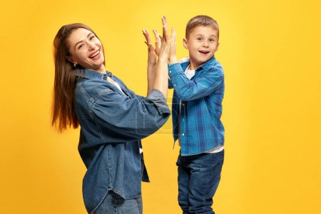 Photo for Mothers support and care. Happy family, mother and son giving high-five and smiling against yellow studio background. Concept of happiness, Mothers day, childhood, fashion and lifestyle - Royalty Free Image
