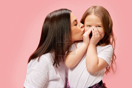 Foto de Hermosa, mujer joven cariñosa, madre besando a su linda niña tierna, hija contra el fondo del estudio rosa. Concepto de felicidad, Día de las Madres, infancia, moda y estilo de vida - Imagen libre de derechos