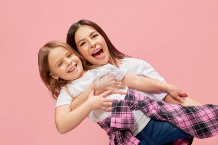 Téléchargez les photos : Mère heureuse jouant avec sa petite fille, famille riant, ayant du bon temps positif sur fond de studio rose. Concept de bonheur, Fête des mères, enfance, mode et mode de vie - en image libre de droit