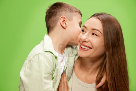 Photo for Little boy, son whispering to mothers eyes against green studio background. Happy, smiling woman with adorable son. Concept of happiness, Mothers day, childhood, fashion and lifestyle - Royalty Free Image