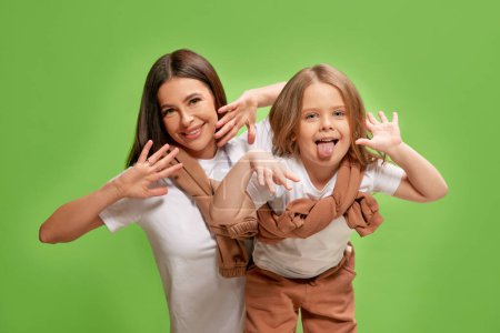 Photo for Same style clothes. Happy, positive mother and her little adorable daughter posing against green studio background. Concept of happiness, Mothers day, childhood, fashion and lifestyle - Royalty Free Image