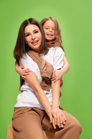 Photo for Happy, beautiful, smiling young woman, mother hugging with cute, tender little girl, daughter against green studio background. Concept of happiness, Mothers day, childhood, fashion and lifestyle - Royalty Free Image