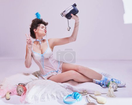 Photo for Beautiful young woman in elegant lingerie, stylish hairstyle sitting on bed and recording video with vintage camera. Blogging lifestyle. Concept of beauty and fashion, vintage, boudoir style - Royalty Free Image