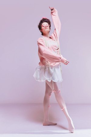 Téléchargez les photos : Belle jeune femme dans de jolis vêtements confortables dansant comme la ballerine encore fond rose pastel. Hobby, esthétique. Concept de beauté et de mode, vintage, style boudoir - en image libre de droit