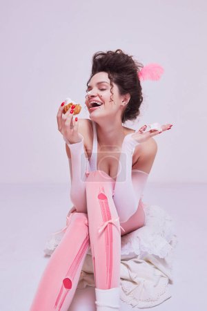 Photo for Happy laughing young woman with stylish hairstyle sitting on floor and eating cake. Birthday celebration promotional photoshoot. Concept of beauty and fashion, vintage, boudoir style - Royalty Free Image