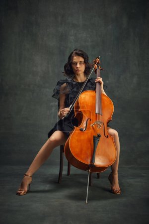 Photo for Female celloist sitting with cello on dark green background. Book cover for musicians memoir, emphasizing personal and artistic growth. Concept of classical art, retro style, music, inspiration - Royalty Free Image