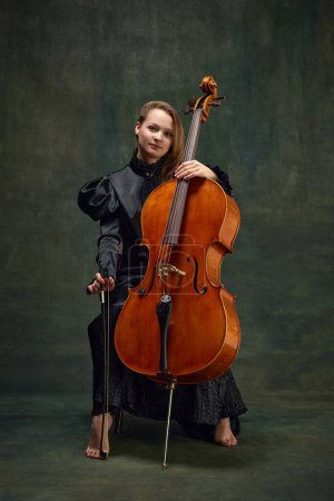 Female celloist sitting with cello on dark green background. Cover for upcoming music events, solo performance of classic melodies. Concept of classical art, retro style, music, inspiration