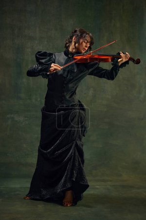 Pose dynamique de musicienne passionnée, jeune femme, violoniste en tenue noire, jouant du violon avec une expression intense sur fond vert vintage. Concept d'art classique, style rétro, musique
