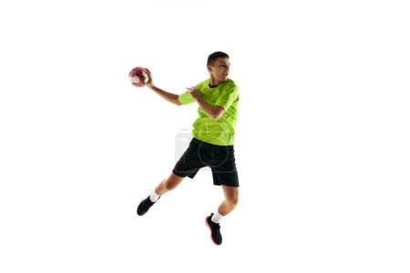 Foto de Joven chico competitivo en uniforme, jugador de balonmano en un salto, lanzando pelota durante el juego contra fondo de estudio blanco. Concepto de deporte profesional, torneo, competición - Imagen libre de derechos